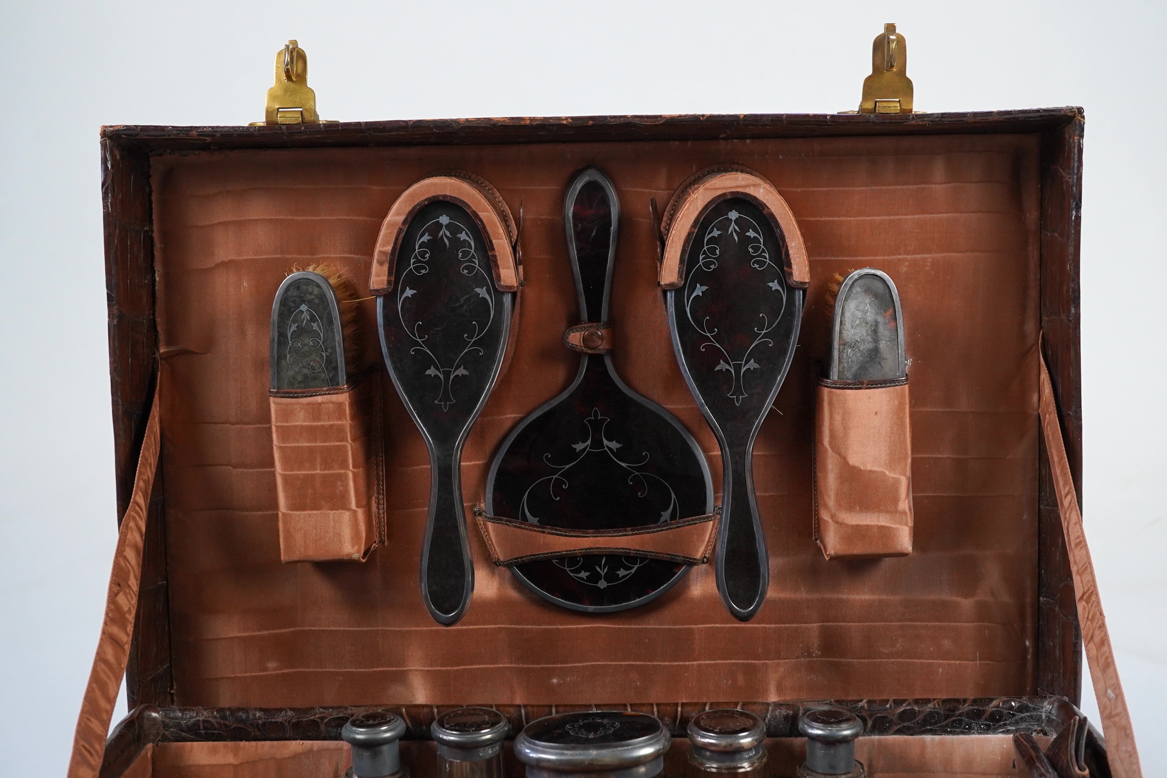 A George V crocodile skin travelling toilet case, containing twelve silver and tortoiseshell mounted accoutrements, by Collet & Anderson